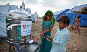 Displaced children wash their hands outside a public toilet at a camp in Sindh Province, Pakistan.