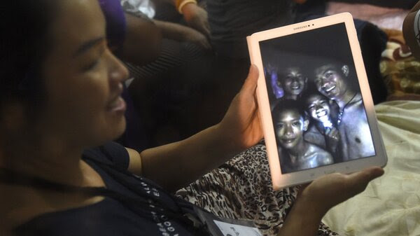 A happy family member shows the latest pictures of the missing boys taken by rescue divers inside Tham Luang cave when all members of children's soccer team and their coach were found alive on Monday.