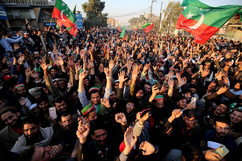 A large group of people rally outside with flags, their hands raised up.