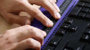Close-up of hands typing on a braille keyboard.