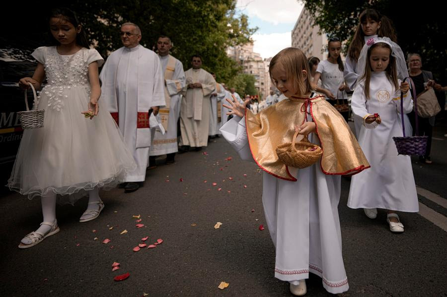 Children throw flower petals as Catholic worshipers and priets walk during a Corpus Christi procession. They are all wearing white clothing.