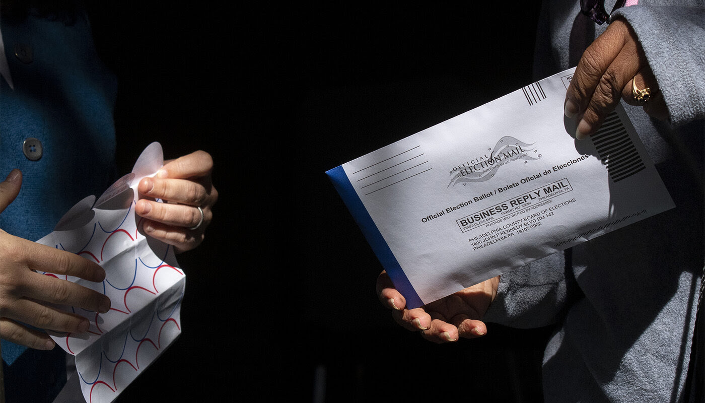 Two people's hands holding, one holding an Official Election Ballet, the other stickers