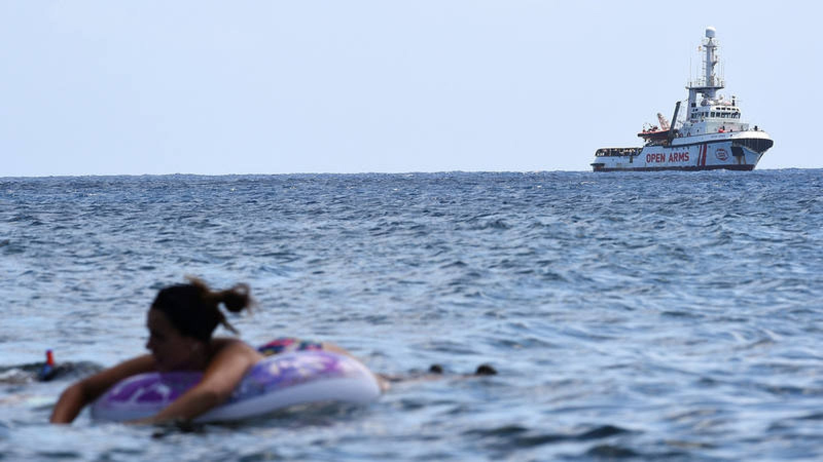 El barco de Open Arms, frente a la costa de Lampedusa, con bañistas en primer término. REUTERS/Guglielmo Mangiapane 