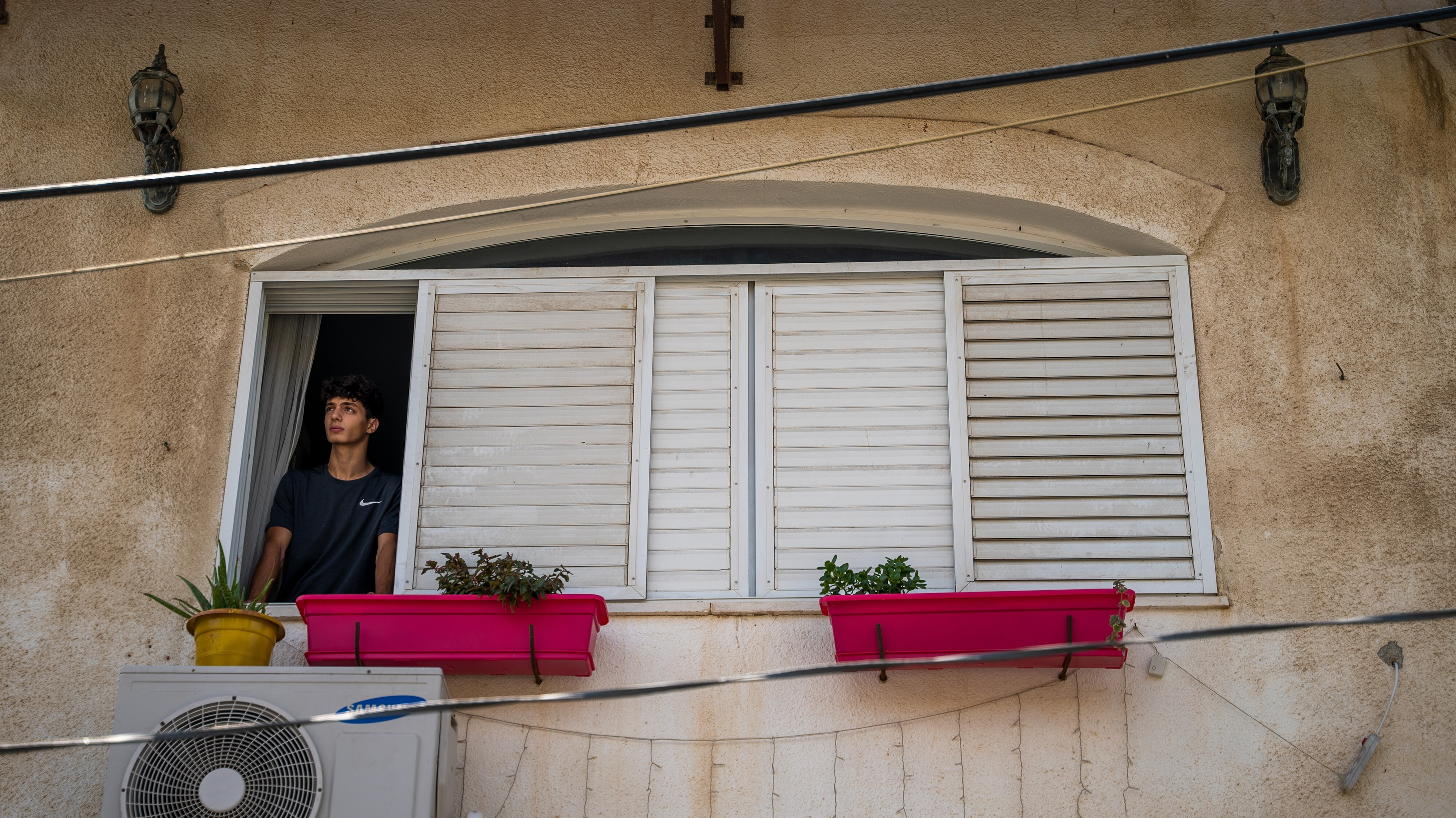 Khalil stands in the window of his home, looking out.