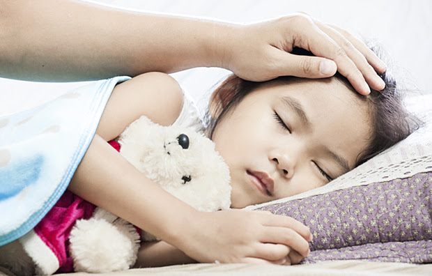 A sick child sleeping while being comforted by a parent.