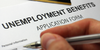 Close-up of a hand with a pen filling in an unemployment benefits application form.