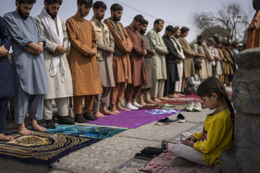 An Afghan girl working as a shoe cleaner sits in the street while men pray during Friday prayers in Kabul, Afghanistan, Friday, Sept. 24, 2021.