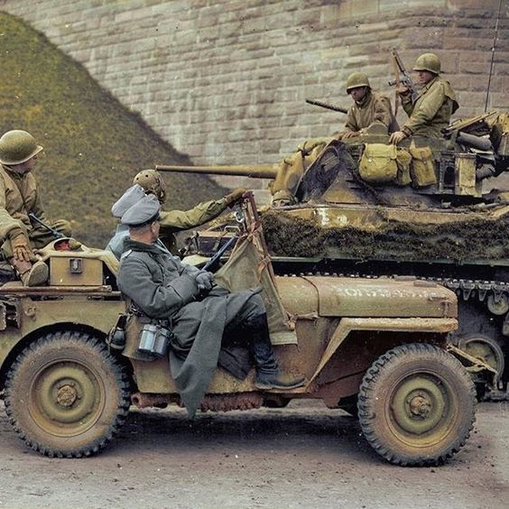 Two high-ranking German Wehrmacht officers being transported under the watchful eye of soldiers from the 4th Armored Division in a Ford GPW jeep, pass by a camouflaged M5 Stuart light-tank belonging to the 37th Armored Regiment during the surrender in Hersfeld, Germany, 31st of March, 1945.