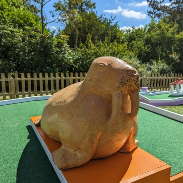 A carved wooden walrus sitting on an orange plinth at one of the putting holes