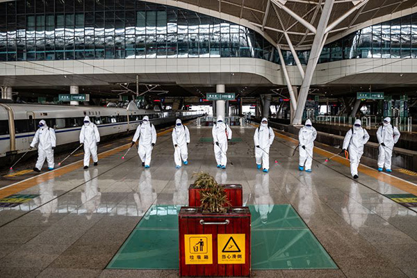 A line of staff in protective overalls spray disinfectant at Wuhan Railway Station