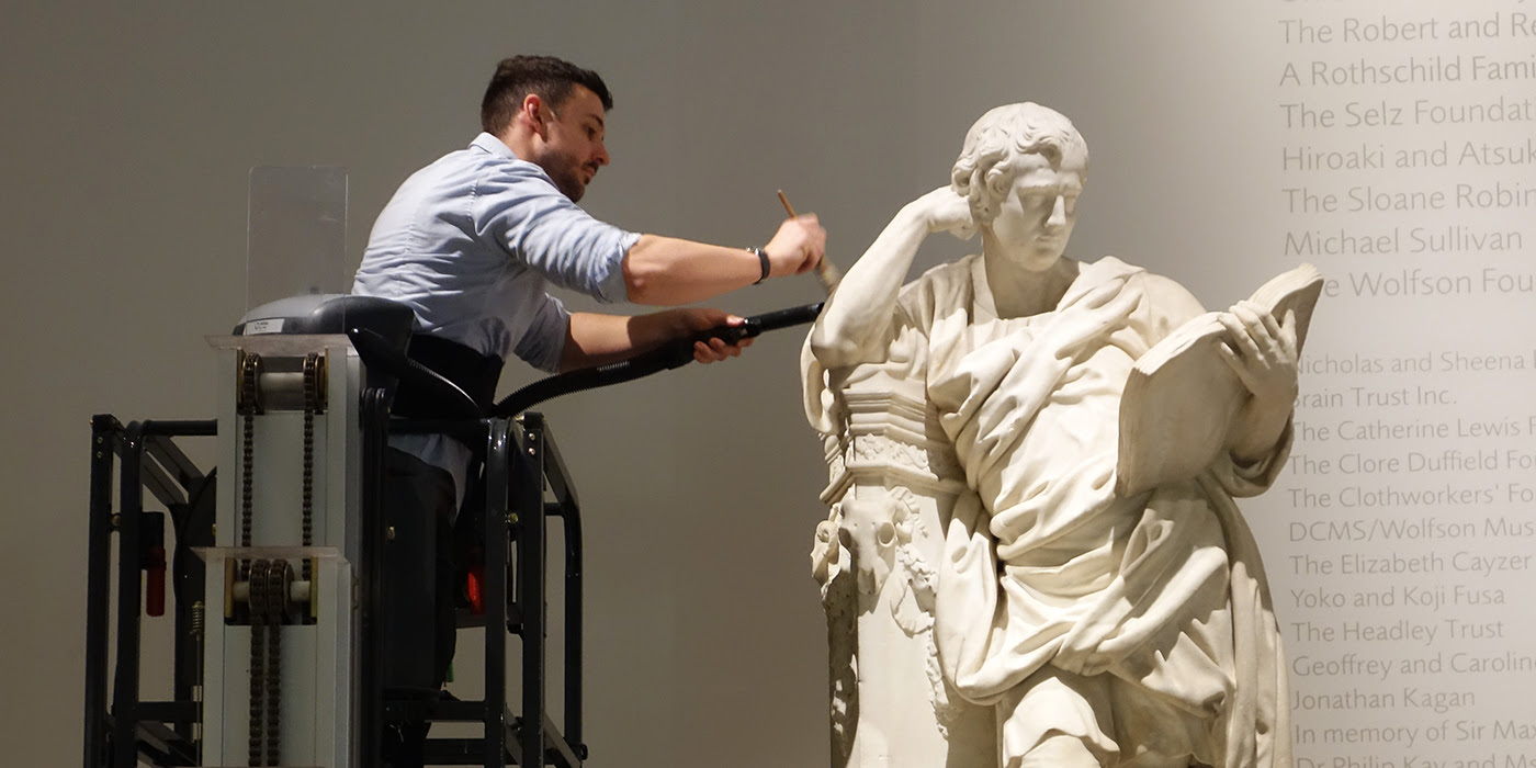 A museum technician brushes dust from a marble statue of a man