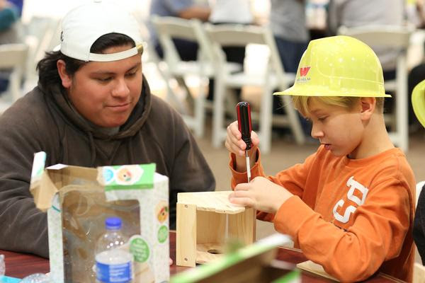 Student works with a student building a birdhouse.