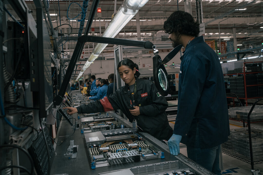 Assembly line workers stand over electronic components.