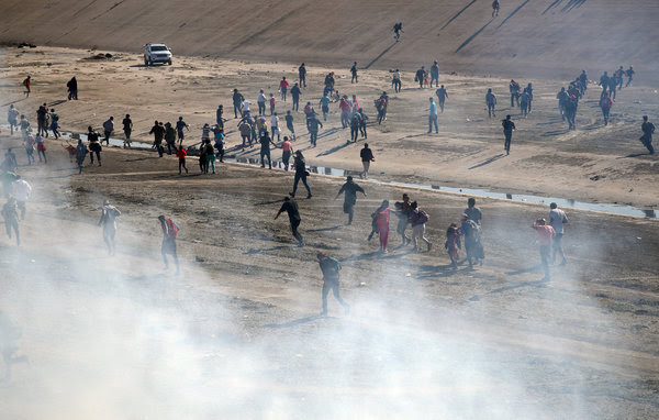 Migrants running from tear gas fired by American border agents near the fence at Tijuana.