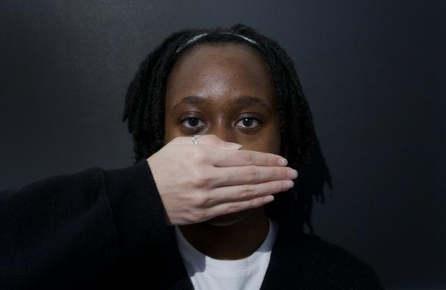 Photo of a Black woman with a White hand covering the lower half of her face.