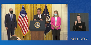 Screen grab of video showing White House event, with Secretary Walsh standing at a podium bearing the presidential seal, flanked by President Biden and AFL-CIO President Liz Shuler, while a sign language interpreter translates. WH.gov 