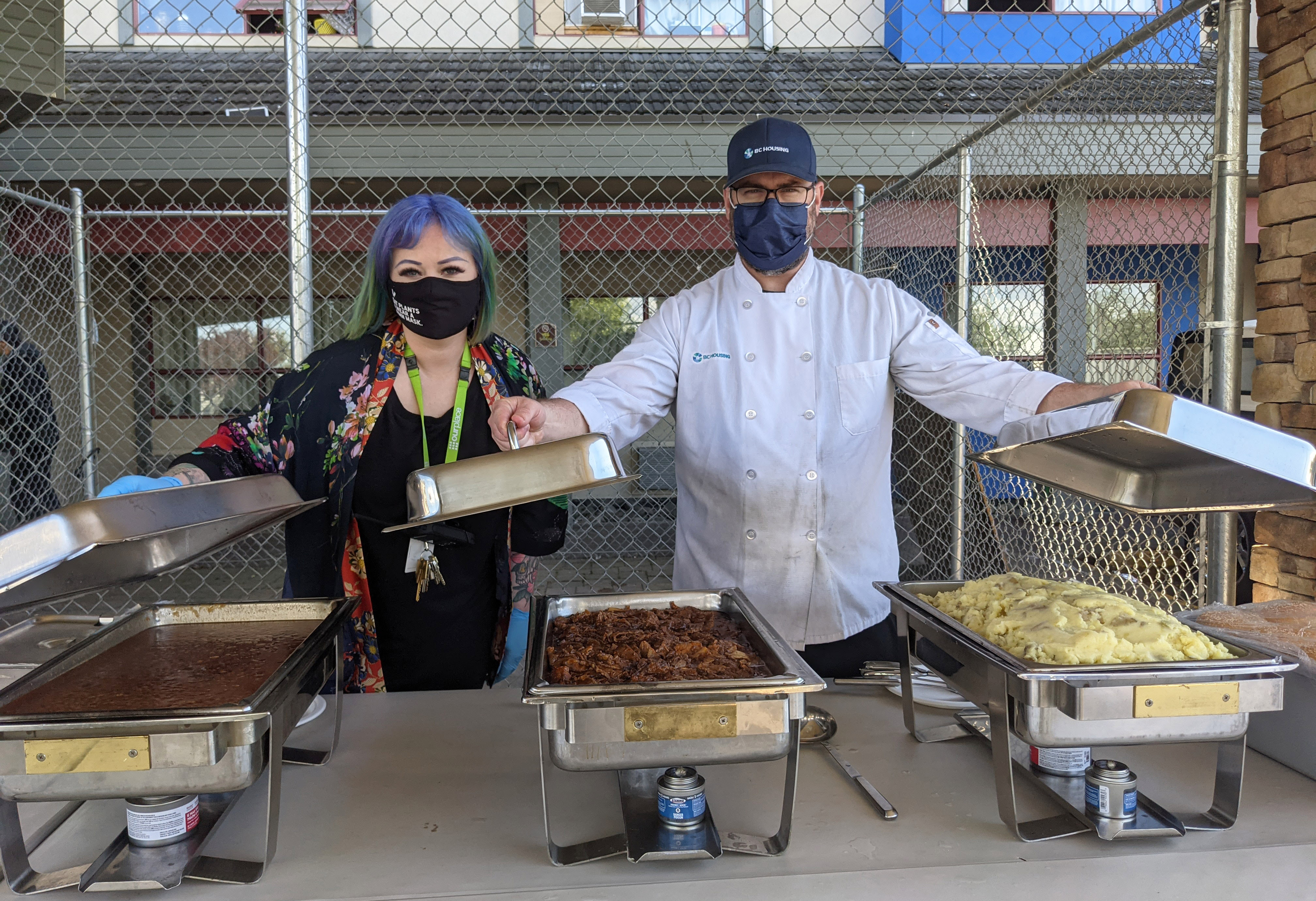 Photo of two volunteers from Our Place ready to serve up some food.