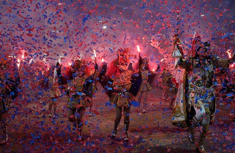 Dancers perform the traditional "Diablada," or Dance of the Devils, during Carnival on Oruro, Bolivia. There are people dancing in costumes while multicolored confetti falls from above.