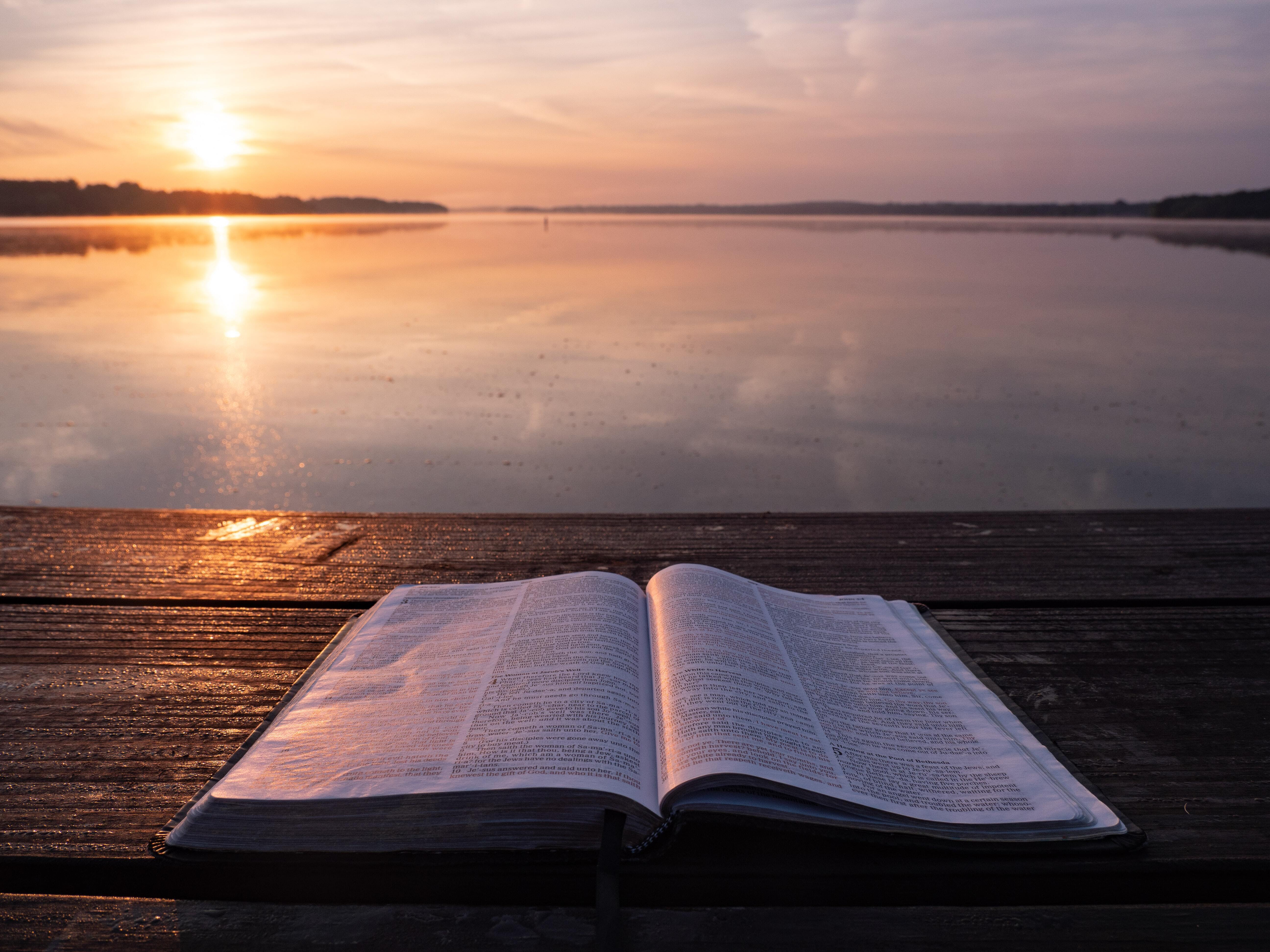 Photo of an open book on a dock overlooking a lake, with the sun setting.