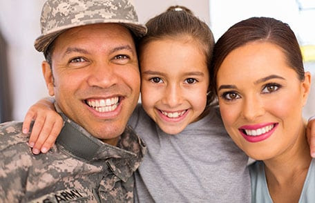 Foto de primer plano del soldado uniformado con su esposa y su hija de 10 años. Hija entre sus padres y abrazándolos mejilla a mejilla. Todos están sonriendo.