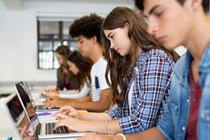 Multiethnic college students sitting in a classroom studying on laptop during class. 