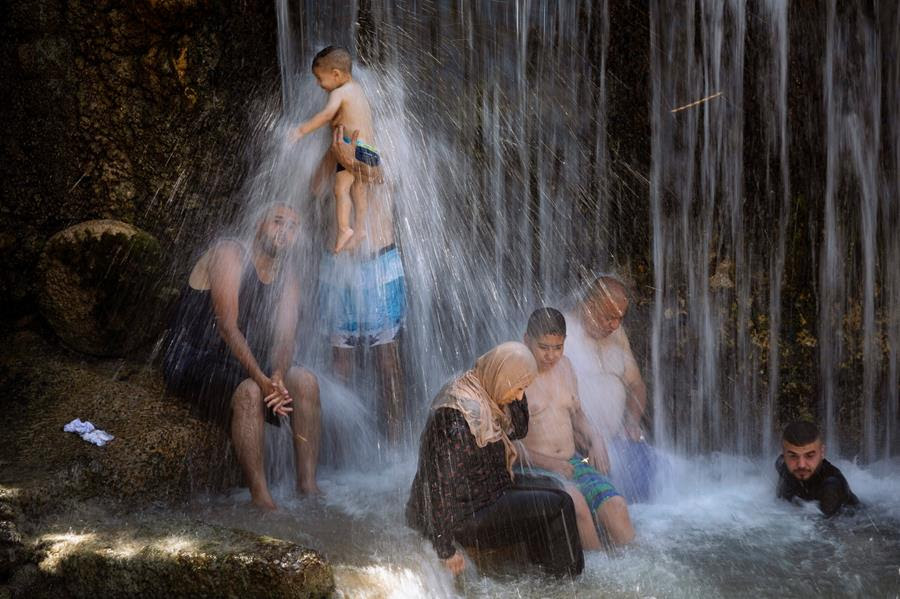 Israeli Arabs stand under a waterfall during the Muslim Eid al-Adha holiday at the Gan HaShlosha national park near the northern Israeli town of Beit Shean, Wednesday, July 21, 2021. Eid al-Adha meaning "Feast of Sacrifice," this most important Islamic holiday marks the willingness of the Prophet Ibrahim (Abraham to Christians and Jews) to sacrifice his son.