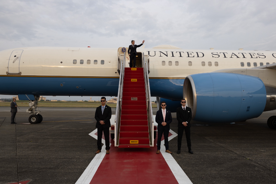 Secretary Blinken waves from the top of airplane stairs.