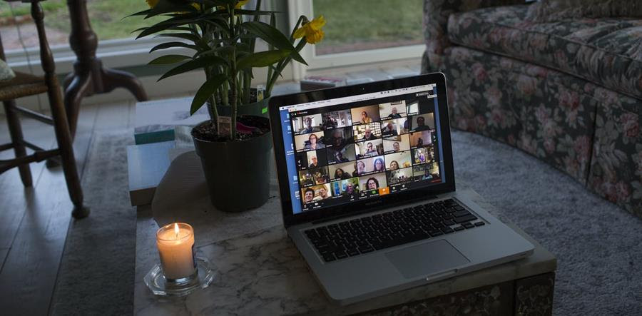 A laptop screen, set on a table, showing a zoom gathering of many people.