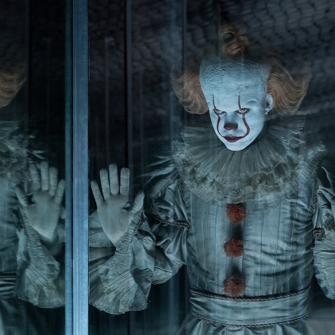 Bill Skarsgård as Pennywise gazes menacingly into a mirror in a hall of mirrors.