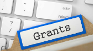 Photo shows a file folder labeled “grants” on top of a computer keyboard. 