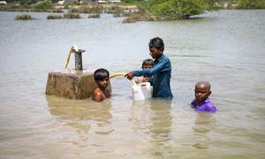 Unos jóvenes recogen agua potable de una línea de suministro de agua bajo el agua de las inundaciones en la provincia de Sindh, Pakistán.