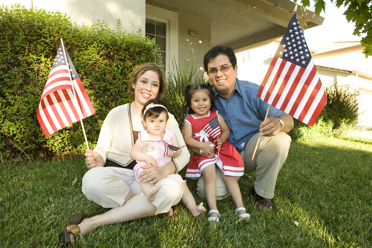 Familia hispana padre, madre y dos hijas bebés levantando banderas de Estados Unidos.Husband, wife and two daughters holding American flag