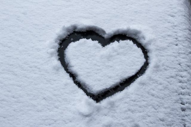 Photo of a snowy windshield - some of the snow has been scraped away into a heart shape.