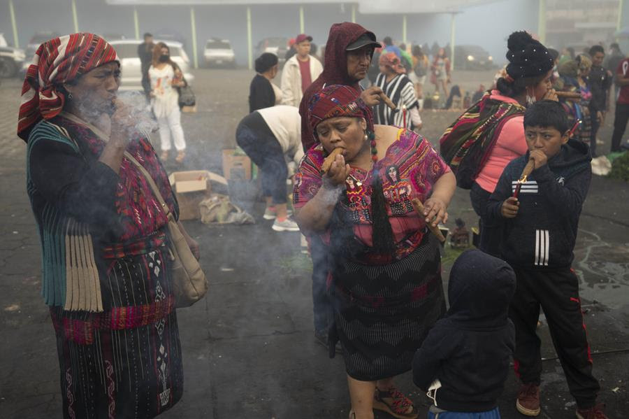 An Indigenous family smokes tobacco as part of a ritual in honor of folk saint Maximon, a fictitious Indigenous person who is a syncretism of a Mayan and Saint Judas Thaddeus, on the feast day of both men outside the Maximon chapel in San Andres Itzapa, Guatemala, Thursday, Oct. 28, 2021. For the second year in a row, the celebration has been reduced amid restrictions to help curb the spread of the COVID-19. (AP Photo/Moises Castillo)