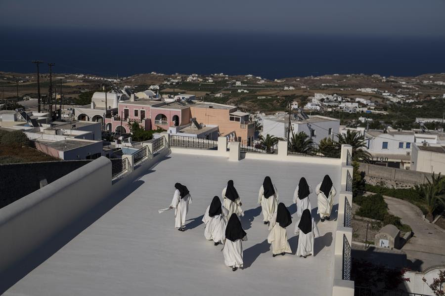 A group of nuns with white habits and dark fails walk together on a terrace.