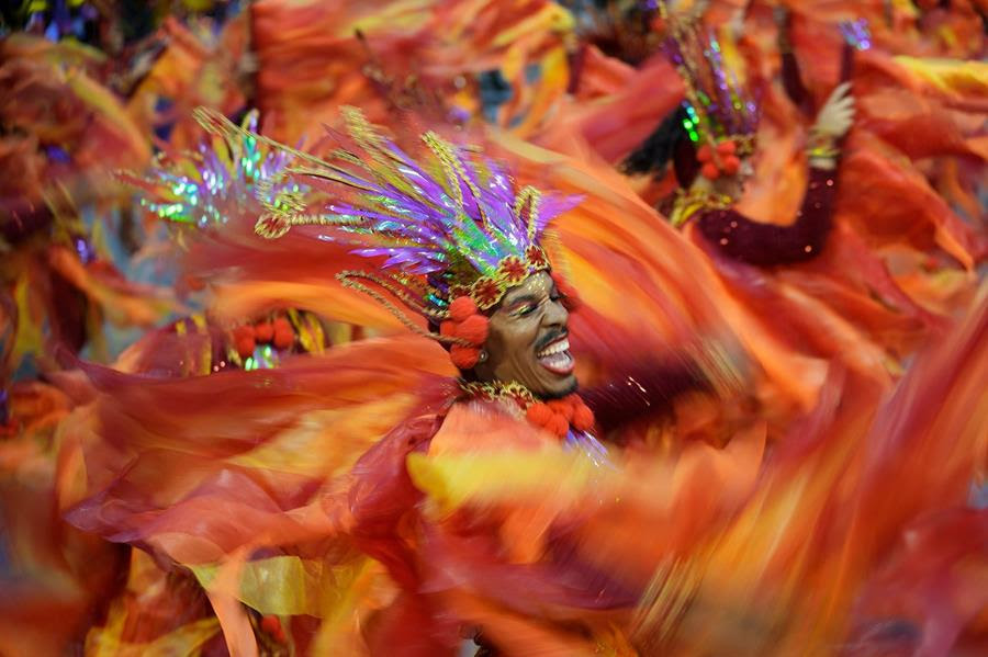 A dancer from Dragoes da Real samba school performs during a carnival parade in Sao Paulo, Brazil. They are wearing brightly colored clothes that blur with motion.