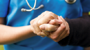 Close-up of a medical professional, wearing scrubs and a stethoscope, clasping the hand of an elderly patient.  
