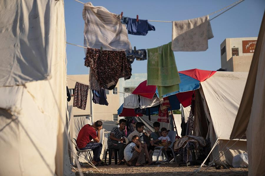 Palestinians displaced by Israeli bombardment of the Gaza Strip sit in a UNDP-provided tent camp. There is laundry drying on ropes hung between the tents.