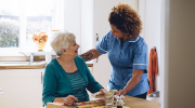 A care worker gives an older woman dinner in her home. 