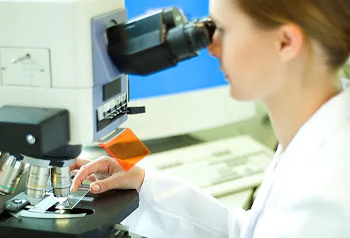 Young female scientist placing slide in microscope