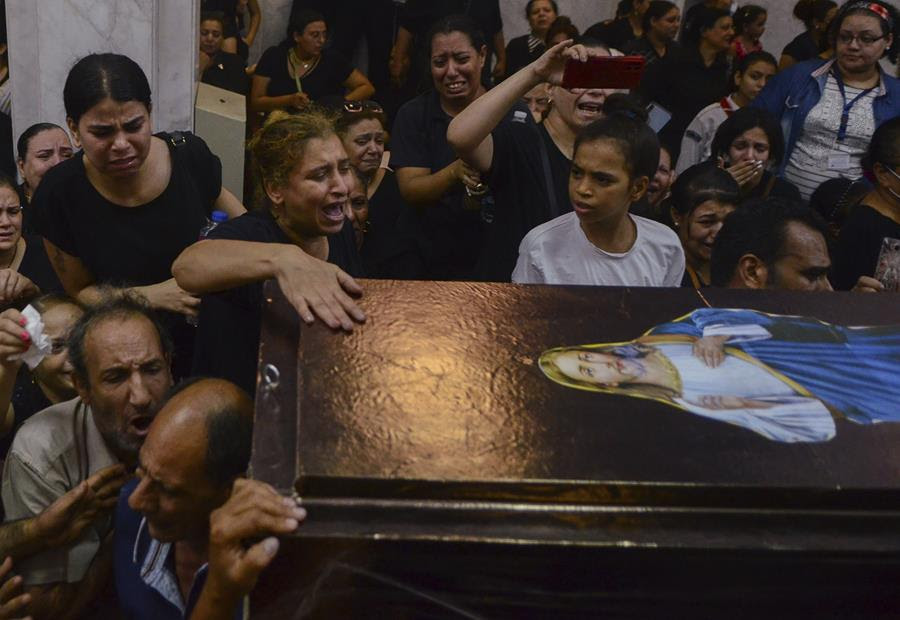 People mourning at a funeral. They are gathered around a coffin with an image of Jesus on it.
