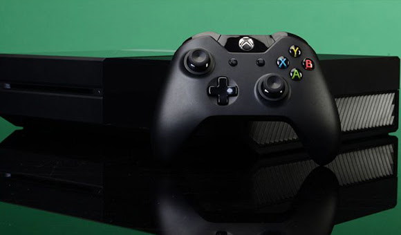 Xbox One X and controller in front of a green background.