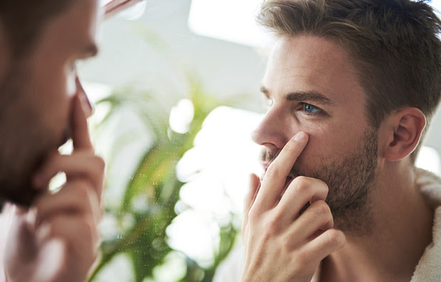 A man examining his eye in the mirror.