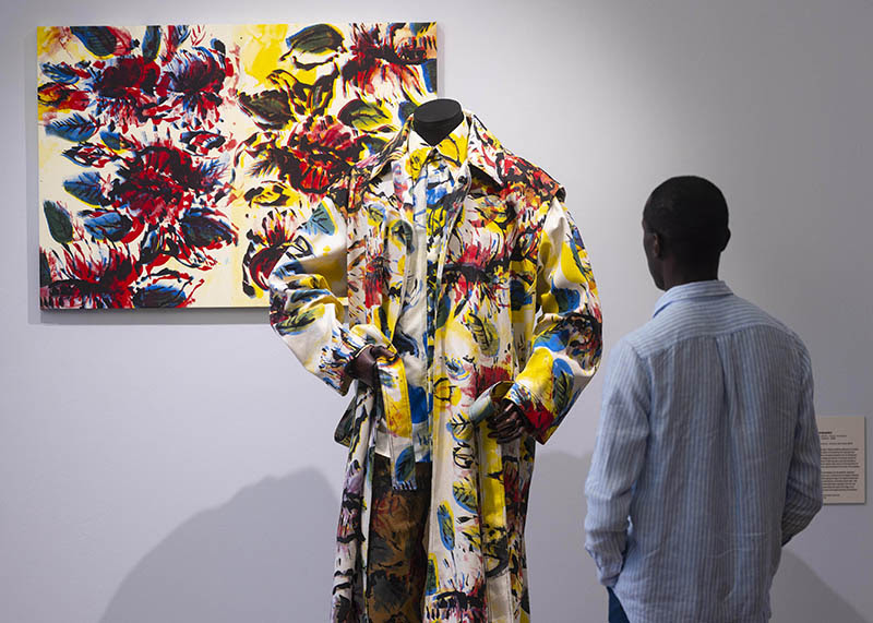 A man looks on at two Bianca Saunders works in the exhibition The Missing Thread. The works include a bright coloured print mounted on a wall and a mannequin wearing clothing designed in the same vivid print.