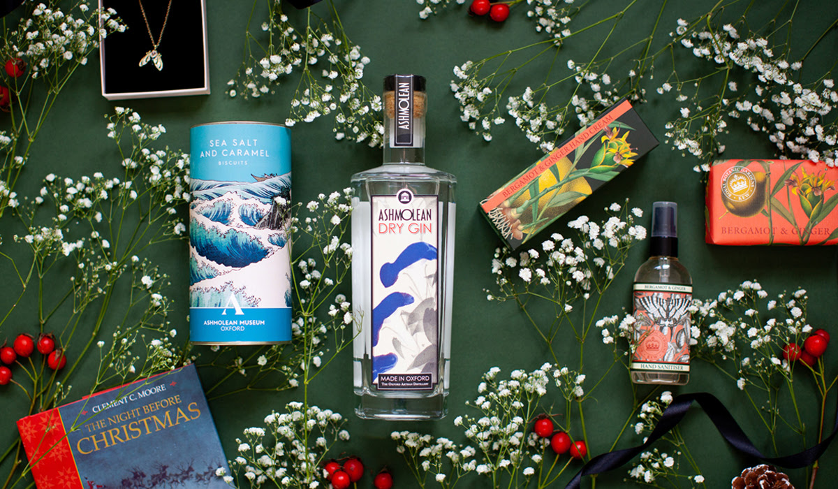 Selection of Ashmolean Christmas shop products on a green background, including Ashmolean gin, biscuits, and soaps
