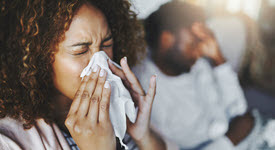 women blowing her nose; man holding his head in pain