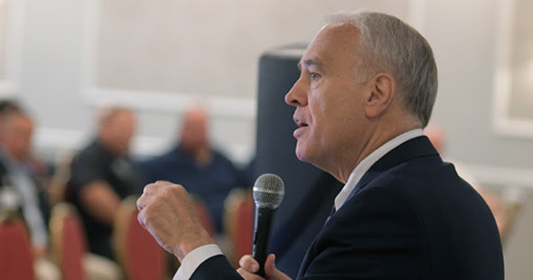 State Comptroller Thomas P. DiNapoli standing at a podium addressing a room filled with people.