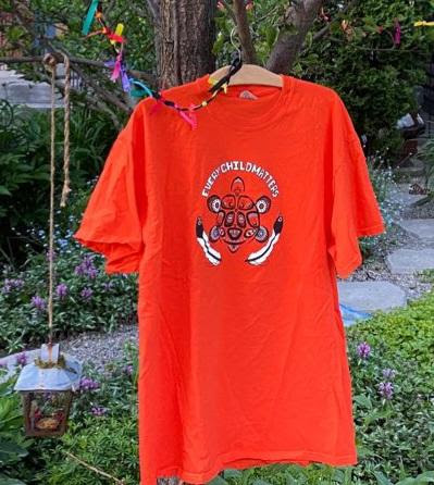 A photo of a bright orange shirt hanging from a tree in a garden.
