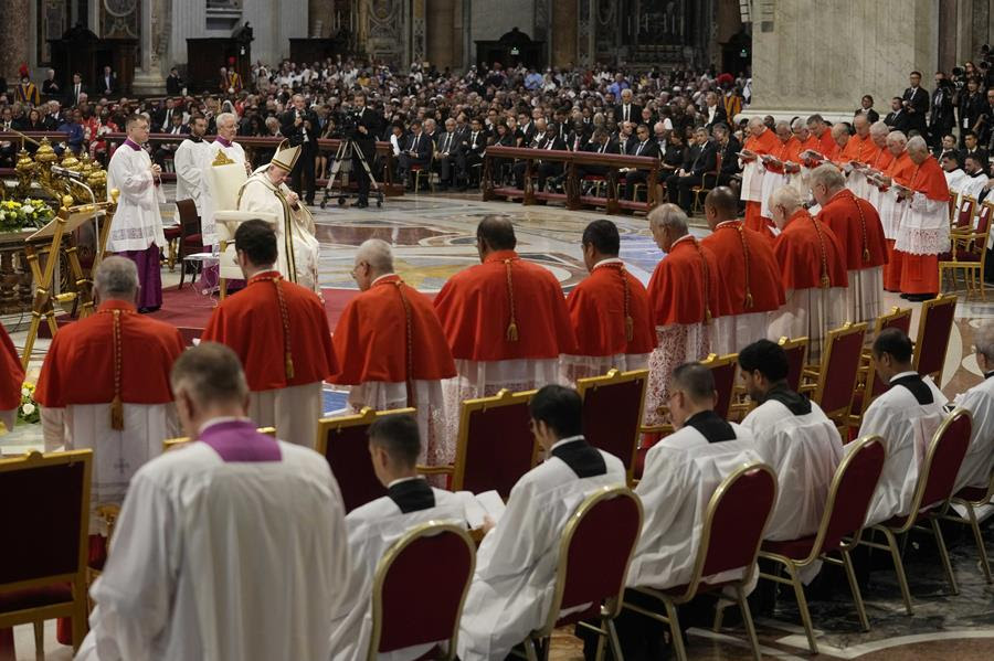 Pope Francis is seated praying in front of people gathered inside St. Peter's Basilica. In the front row are the Catholic Church's 20 newest cardinals.