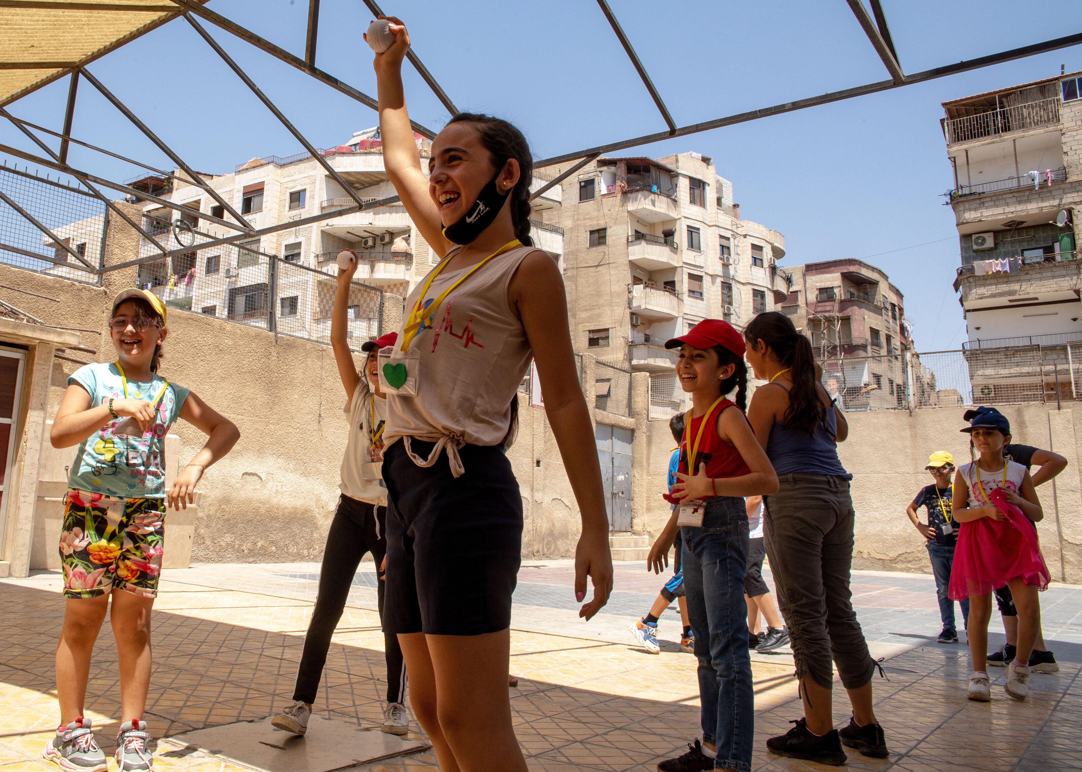Children playing in school yard surrounded by cement walls, with apartment buildings behind.